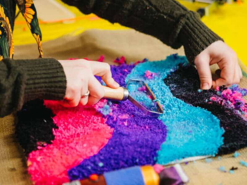 Person shaving a colourful tufted rug
